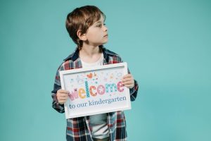 Adorable child holding a 'Welcome to our kindergarten' sign against a turquoise background.