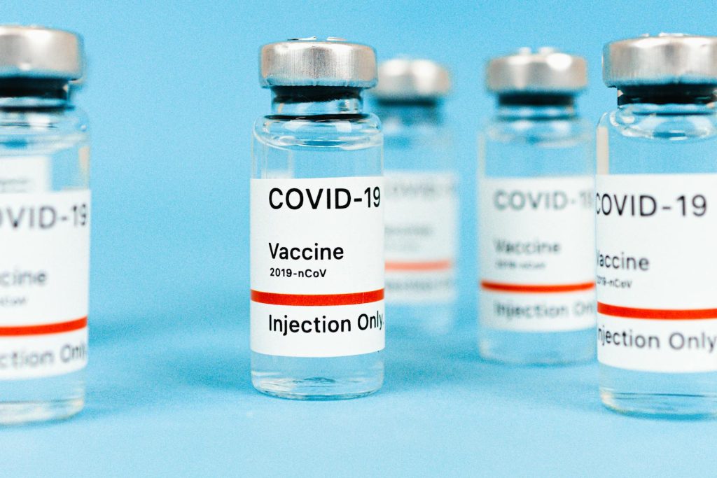 Close-up of COVID-19 vaccine vials with label and liquid on a light blue background.
