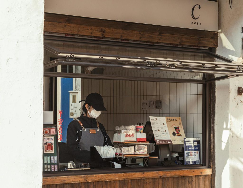 A worker behind the counter of an outdoor cafe kiosk, preparing orders.