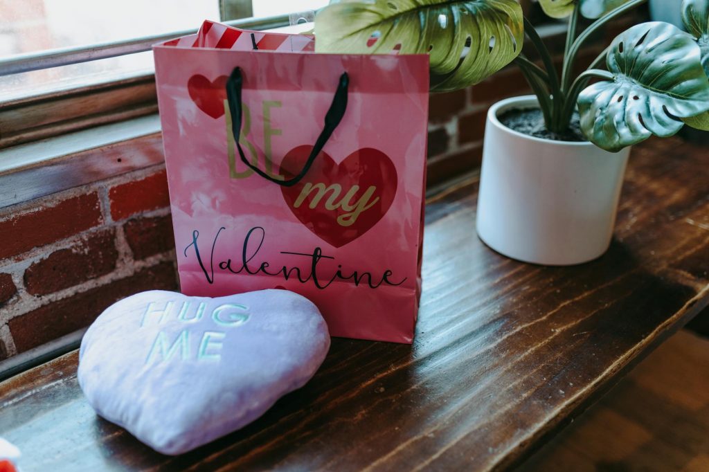 A romantic Valentine's Day gift setup featuring a bag and pillow on a wooden table indoors.