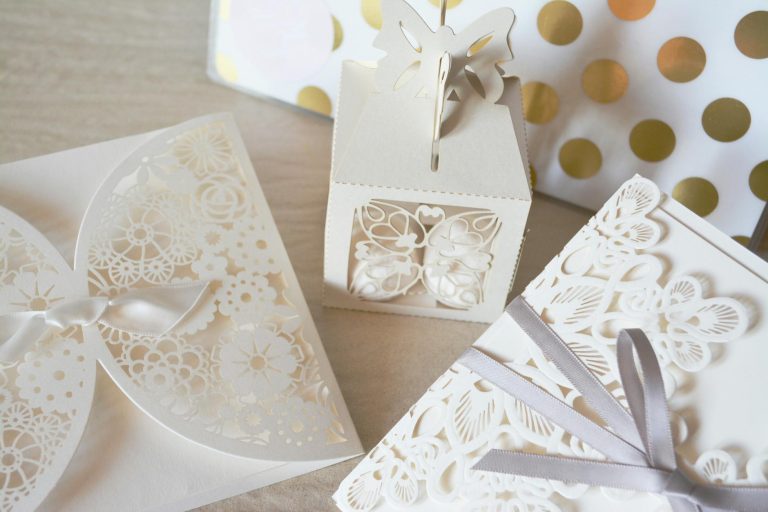 Beautiful laser cut invitations and gift box with intricate designs and ribbons, perfect for weddings or special events.
