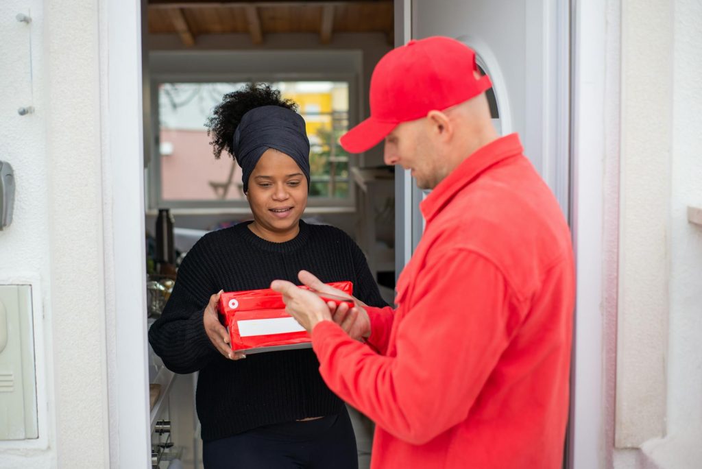 A courier hands a package to a smiling woman at her home entrance, symbolizing efficient delivery service.