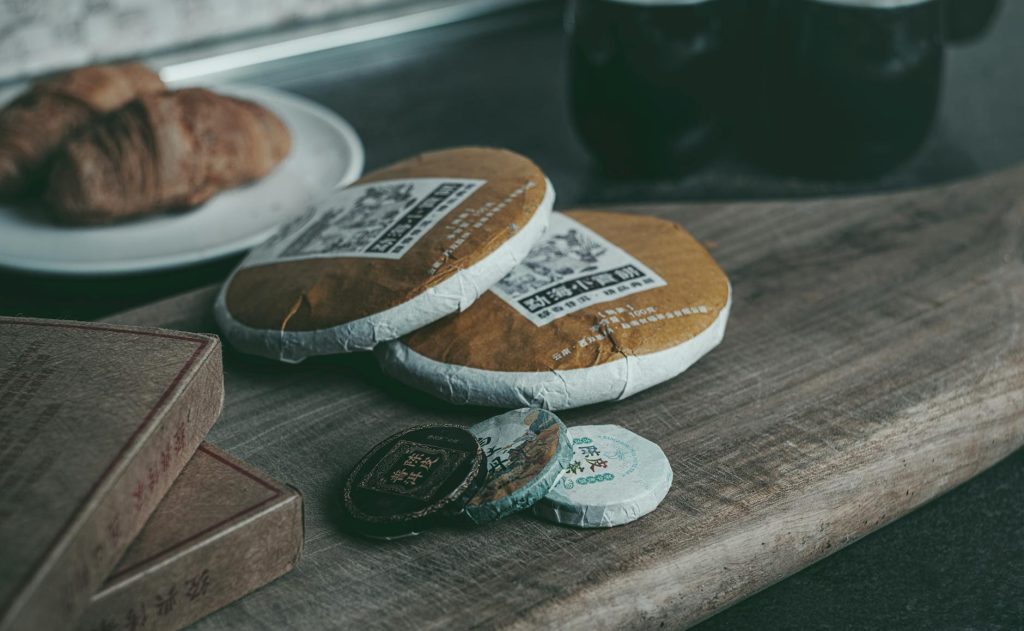 Still life showcasing traditional tea packaging with a croissant on wooden board, evoking a cozy atmosphere.