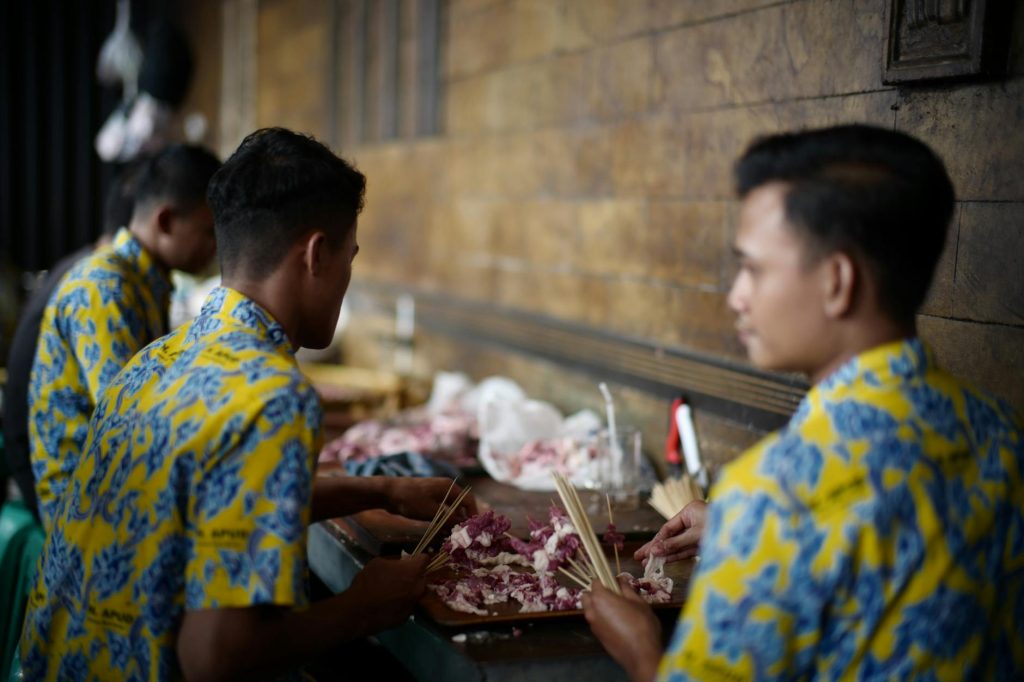 Men in yellow shirts preparing skewers at a Jakarta restaurant.