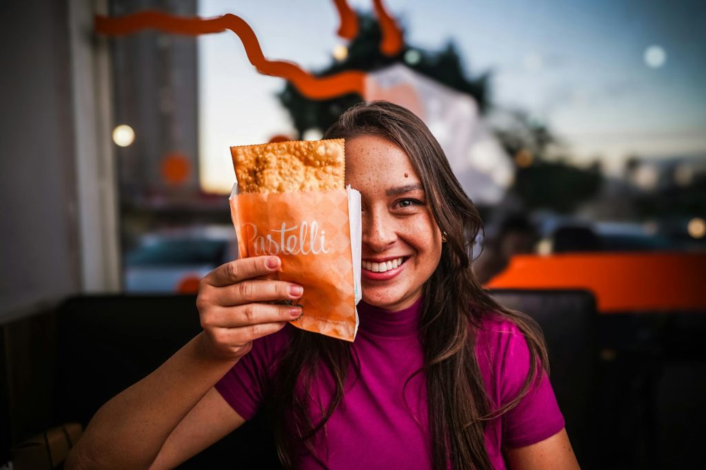 Young woman enjoying a fried pastry in a vibrant cafe setting.