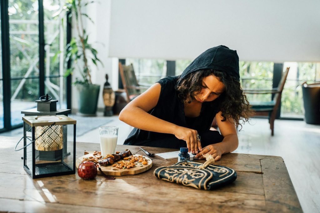 Woman engaged in artistic work at home, surrounded by snacks and decor, creating a peaceful vibe.