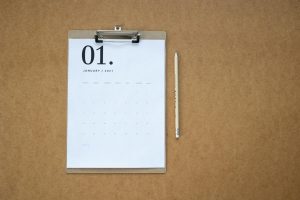 Flat lay of a January 2021 calendar on a clipboard with a pencil on brown background.