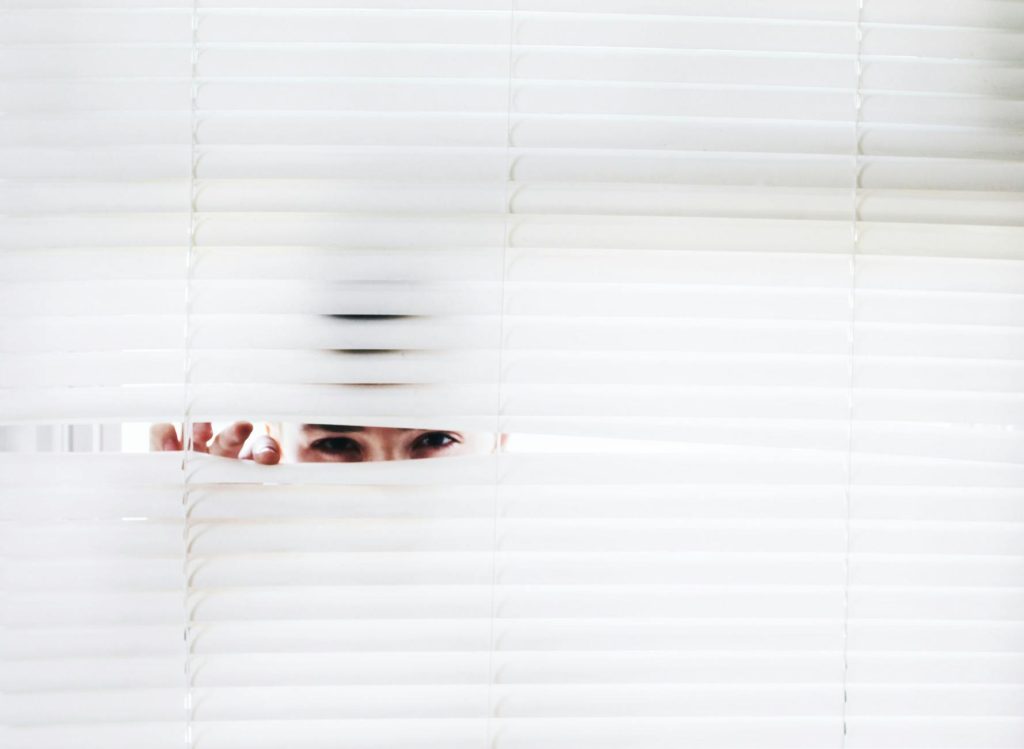 A person peeks through white blinds, creating an intriguing sense of curiosity.