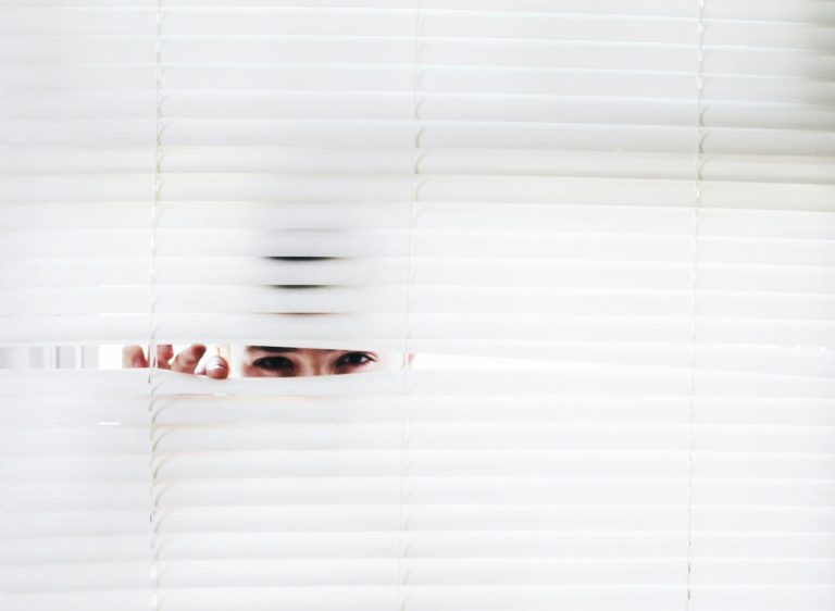 A person peeks through white blinds, creating an intriguing sense of curiosity.