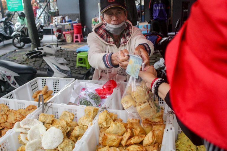 Street vendor sells traditional snacks at urban market, exchanging cash.