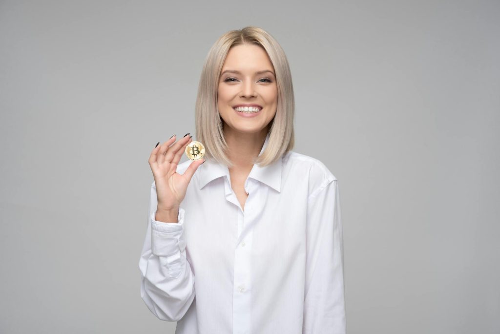 A cheerful woman displaying a bitcoin, embodying digital currency and modern finance.