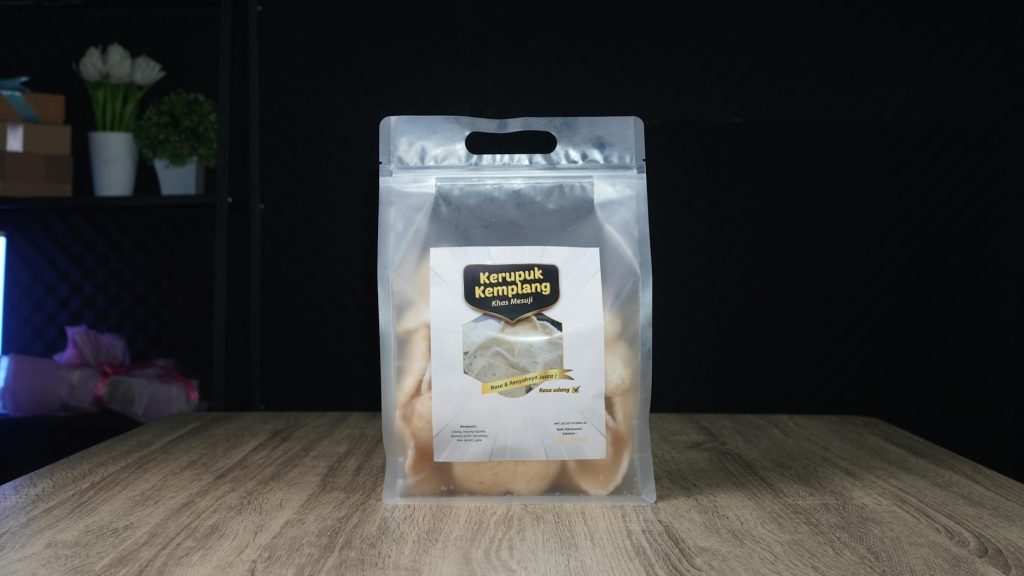 Clear packaging of Kerupuk Kemplang shrimp crackers on a wooden table.