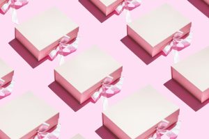 Aesthetic pink gift boxes with ribbons in a seamless pattern on a pink background.