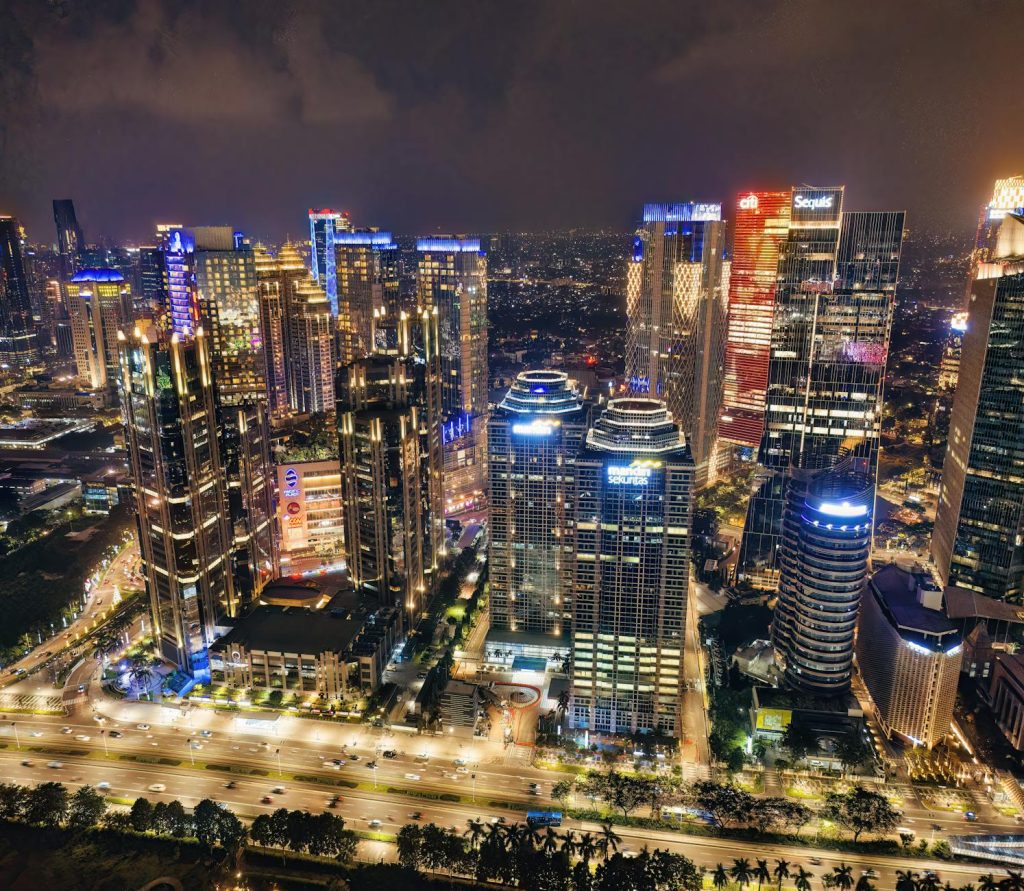A vibrant night skyline of Jakarta, showcasing illuminated skyscrapers and bustling urban life.