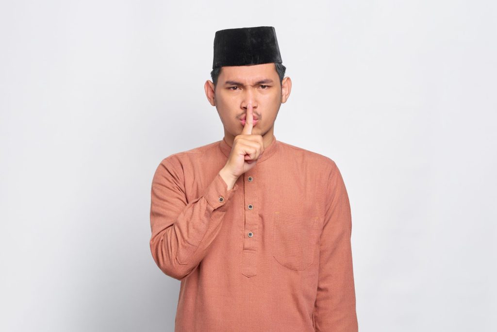 Portrait of a man wearing a kufi, making a silence gesture. Ideal for cultural themes.