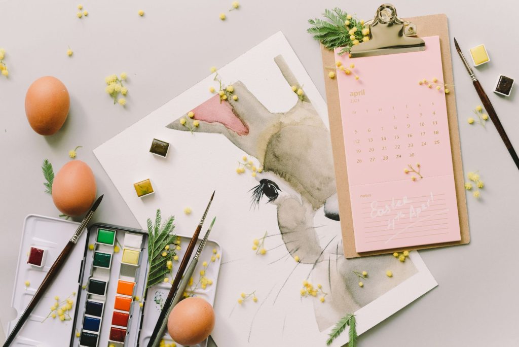 Flat lay of Easter bunny watercolor art, April calendar, eggs, and brushes for a creative spring celebration.