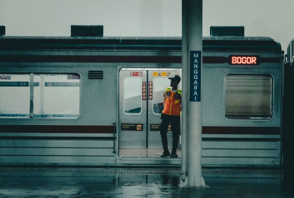 A security officer at Manggarai Station during a rainy day with a train headed to Bogor.