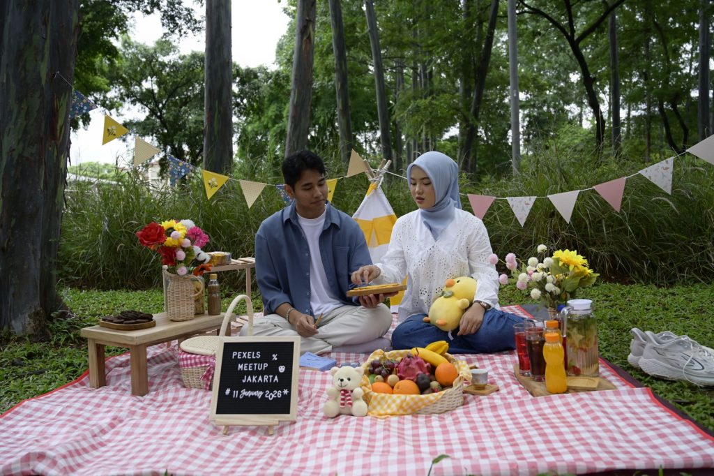 Young couple enjoying a picnic with fruits and drinks in a Jakarta park.