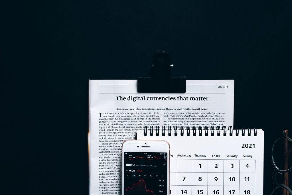 Digital currencies article with smartphone stock market app and calendar on black surface.