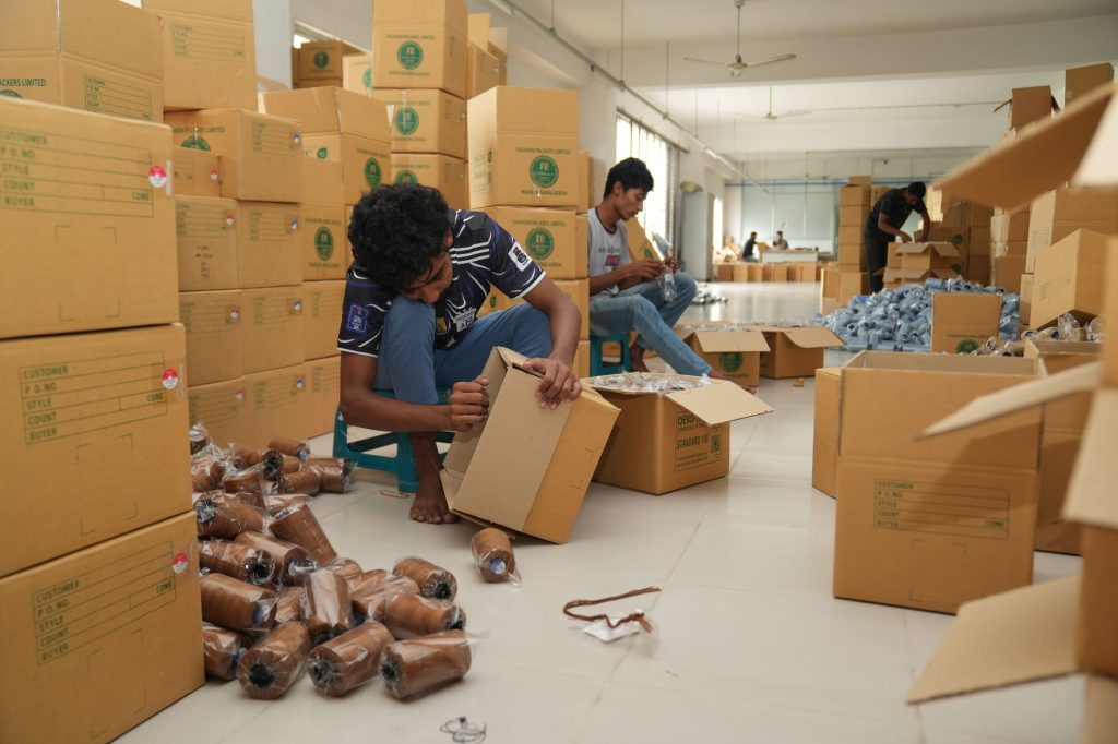 Industrial workers packaging goods in a busy factory environment with numerous cardboard boxes.