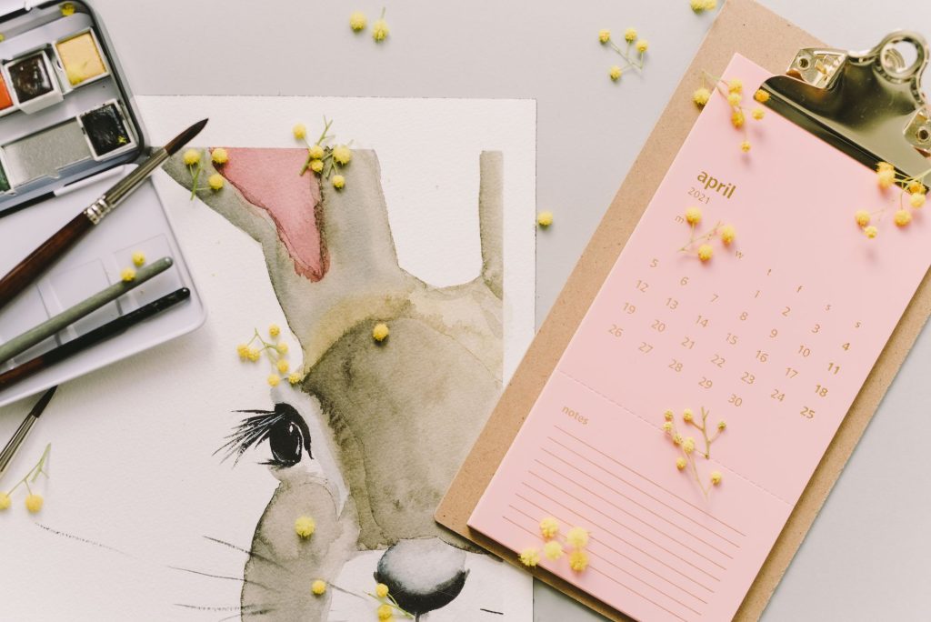 A watercolor bunny painting with April calendar and mimosa flowers.